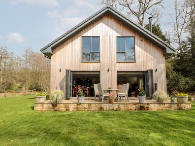 A wooden house with open folding doors leading to a patio with a table and chairs and potted plants on grass at Romsey Lodge in Wark