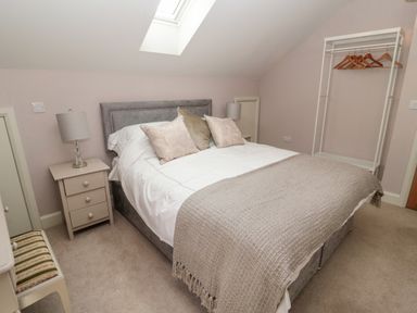 A bedroom with a double bed pillows bedside tables lamps a chair and an open wardrobe at Romsey Lodge in Wark