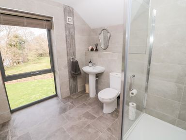 A bathroom with a toilet sink shower and a window showing grass and trees at Romsey Lodge in Wark