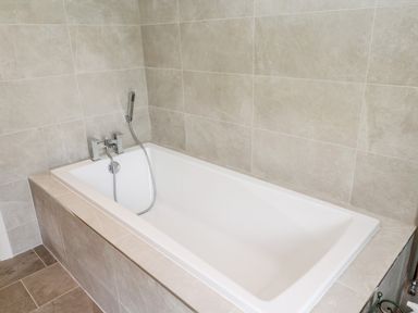 A bathtub with handheld showerhead and tiled walls and floor at Romsey Lodge in Wark