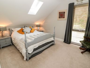 A bedroom with a bed with pillows and two bedside tables with lamps next to a window with blinds and curtains at Romsey Lodge in Wark