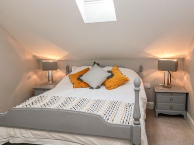 A bedroom with a bed against a slanted wall with bedside tables and lamps at Romsey Lodge in Wark