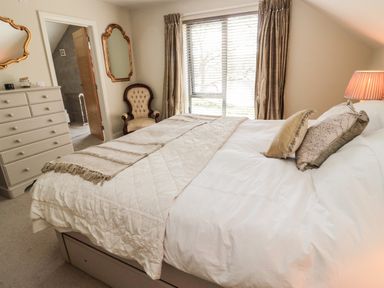 A bedroom with a bed a chest of drawers a window with curtains an armchair and two mirrors at Romsey Lodge in Wark