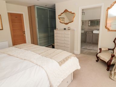 A bedroom with a bed a dresser a wooden door an armchair and an open doorway to a bathroom at Romsey Lodge in Wark