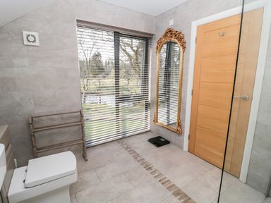 A bathroom with a toilet wooden door a large window with blinds a decorative mirror and a towel rack at Romsey Lodge in Wark