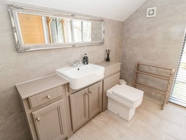 A bathroom with a white sink and toilet a beige cabinet a large rectangular mirror and a wooden towel rack at Romsey Lodge in Wark