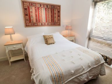 A bedroom with a bed and two bedside tables with lamps a patterned wall hanging and a window with blinds at Romsey Lodge in Wark
