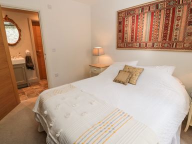 A bedroom with a bed covered in white bedding and two pillows a nightstand with a lamp and a patterned wall hanging above the bed at Romsey Lodge in Wark