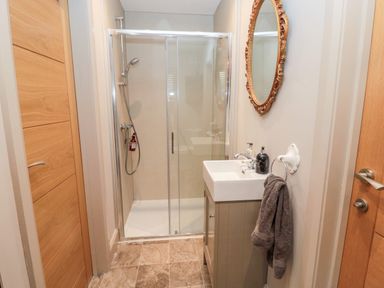 A bathroom with a shower enclosure a sink with toiletries and a mirror at Romsey Lodge in Wark