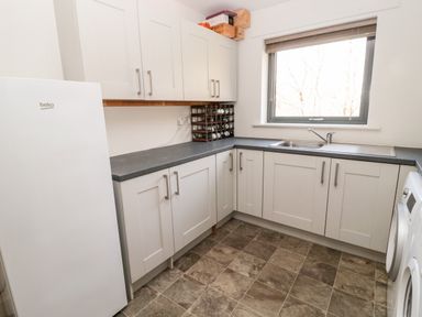 A kitchen with white cabinets gray countertops a white fridge and a window at Romsey Lodge in Wark