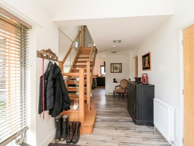A hallway with wooden stairs and coats hanging on a wall rack at Romsey Lodge in Wark