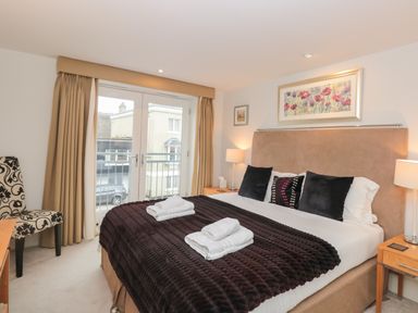 A bedroom with a double bed with dark brown blanket and white towels on it two bedside tables with lamps and a chair near balcony doors at 42 Dart Marina Dartmouth