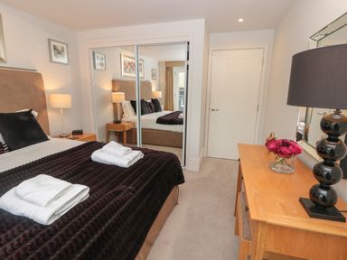 A bedroom with a bed folded towels bedside tables lamps a wooden dresser with a vase of flowers and a lamp at 42 Dart Marina in Dartmouth