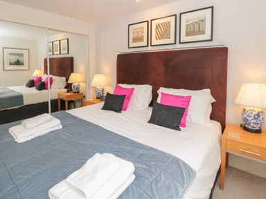 A bedroom with a double bed with pillows and folded towels bedside tables with lamps and a mirrored wardrobe at 42 Dart Marina in Dartmouth