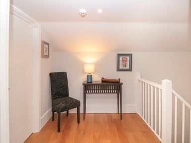 A small sitting area with a black patterned chair a wooden table with a lamp and artwork on white walls at 42 Dart Marina Dartmouth
