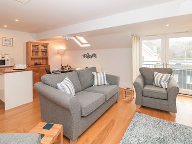 A living room with grey sofas and a wooden floor next to a dining area and kitchen at 42 Dart Marina in Dartmouth