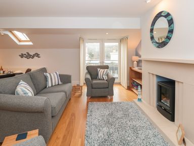 A living room with a gray sofa and armchair a fireplace and glass doors at 42 Dart Marina in Dartmouth