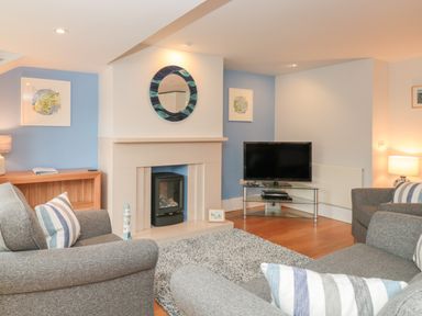 A living room with grey sofas, a fireplace, a TV on a glass stand, and blue accent walls at 42 Dart Marina in Dartmouth