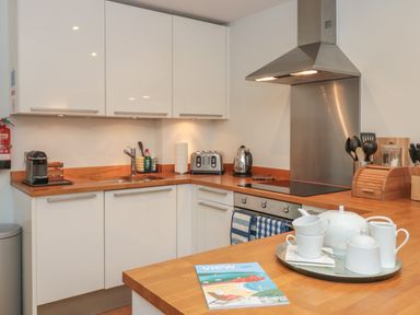 A kitchen with white cabinets wooden countertops a stainless steel oven stovetop and range hood a coffee machine toaster kettle and a tea set on a counter at 42 Dart Marina in Dartmouth