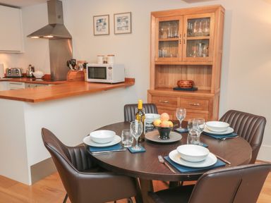A dining area with a round table set with dishes and glasses next to a kitchen counter and wooden cabinet at 42 Dart Marina in Dartmouth