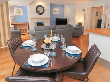 A dining table set with plates glasses and a bowl of fruit in an open living room with sofas and a TV at 42 Dart Marina in Dartmouth