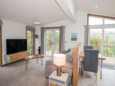 A living room with a sofa table lamp television and dining table with chairs at 1 Valley View in Lanreath
