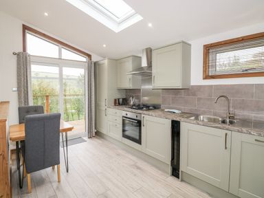 A kitchen with cabinets a dining table and chairs and glass doors opening to a balcony at 1 Valley View in Lanreath