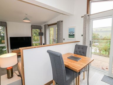 A dining area with a wooden table and two chairs next to a glass door leading outside at 1 Valley View Lanreath