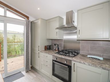 A kitchen with gray cabinets a gas stove an oven a toaster and a kettle with a glass door leading outside at 1 Valley View in Lanreath