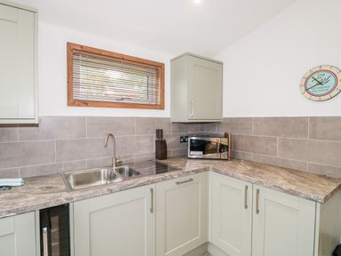 A kitchen corner with a stainless steel sink microwave and wall clock at 1 Valley View in Lanreath