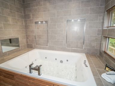 A bathroom with a whirlpool bathtub set into a wooden frame and tiled walls with built-in shelves at 1 Valley View in Lanreath