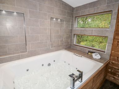 A bathroom with a large whirlpool bathtub and two windows with blinds at 1 Valley View in Lanreath