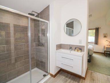 A bathroom with a glass shower enclosure and a white sink with a round mirror at 1 Valley View in Lanreath