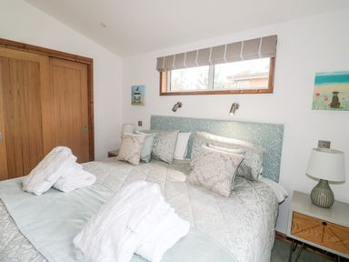A bedroom with a double bed pillows robes bedside tables lamps and a window at 1 Valley View in Lanreath