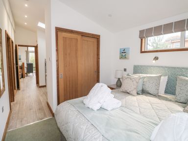 A bedroom with a bed, pillows, robes on bed, wooden closet doors and a window at 1 Valley View in Lanreath