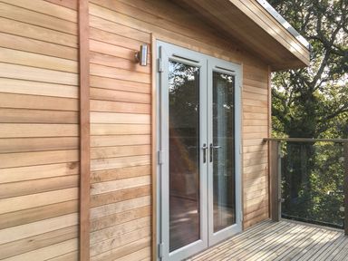 A wooden exterior wall with glass double doors and a glass balcony railing at 1 Valley View Lanreath