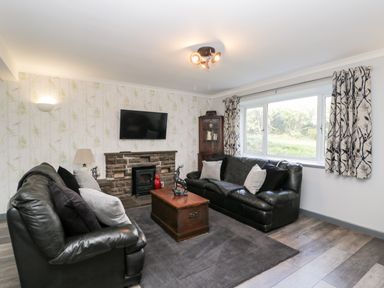 A living room with two black leather sofas cushions a wooden chest coffee table a mounted television and a large window at Pool House in The Narth near Trellech
