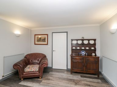 A room with a brown leather armchair and a wooden cabinet with plates and cups at Pool House The Narth near Trellech