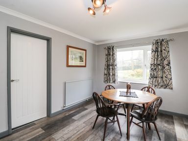 A dining room with wooden table and four chairs a window with patterned curtains and a closed door at Pool House The Narth near Trellech