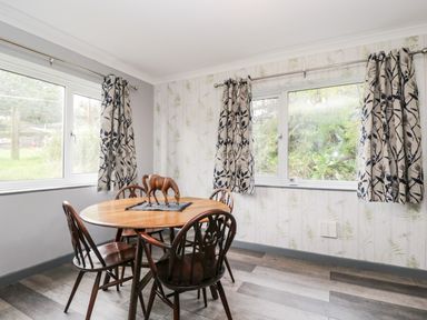A dining area with a round wooden table and four chairs wooden horse figurine on the table windows with patterned curtains at Pool House in The Narth near Trellech