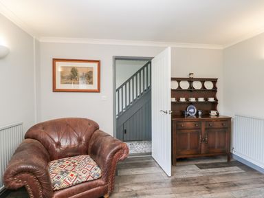 A room with a leather armchair a wooden cabinet with dishes and an open door showing stairs at Pool House The Narth near Trellech