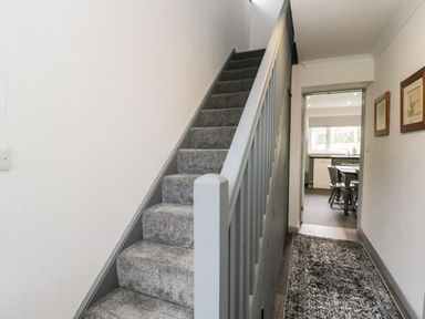 A hallway with carpeted stairs and a patterned runner rug leading to a kitchen with a table and chairs at Pool House The Narth near Trellech
