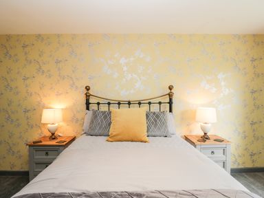 A bedroom with a bed against a floral wallpapered wall with two bedside tables and lamps at Pool House in The Narth near Trellech