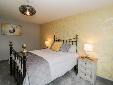 A bedroom with a black metal bed, bedside tables with lamps and floral wallpaper at Pool House The Narth near Trellech