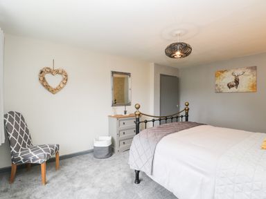 A bedroom with a patterned chair dresser mirror bed and wall art at Pool House The Narth near Trellech