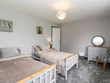 A bedroom with two single beds a dresser with a round mirror a chair and a door at Pool House in The Narth near Trellech