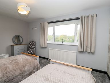 A bedroom with two beds a chair a dresser with a round mirror and a window with curtains at Pool House The Narth near Trellech