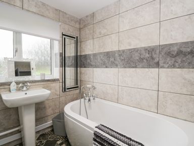 A bathroom with a bathtub a pedestal sink a window and tiled walls at Pool House The Narth near Trellech