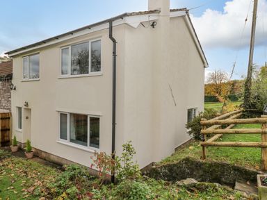 The exterior of a two-story house with white walls and multiple windows surrounded by grass and plants at Pool House The Narth near Trellech