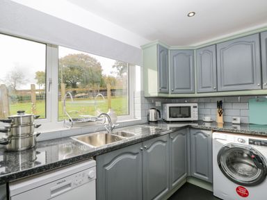 A kitchen with grey cabinets a dishwasher a washing machine a microwave a kettle and a window overlooking a garden at Pool House The Narth near Trellech